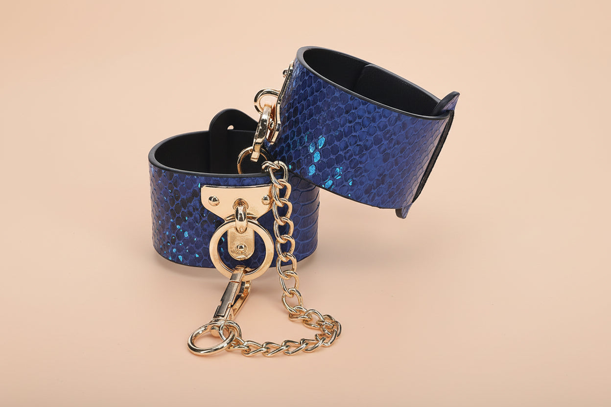 Jewish Joyboxx Blue leather handcuffs, snakeskin texture with gold hardware on a white background